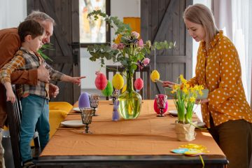 Grandpa, grandson and mother are getting ready for Easter dinner. At the table in the house, beside a decoration of paper eggs.
