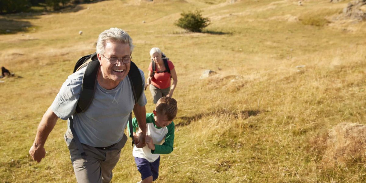 Grandparents With Grandchildren Climbing Hill On Hike Through Countryside In Lake District UK Together