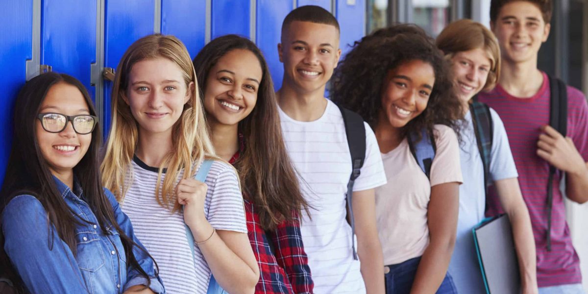 Teenage school kids smiling to camera in school corridor