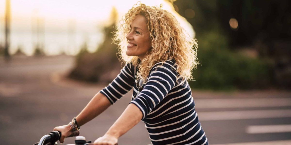 Cheerful beauiful blonde curly caucasian woman smile and enjoy the ride on a bike in outdoor leisure activity in the city - free and joyful active people on the street having fun