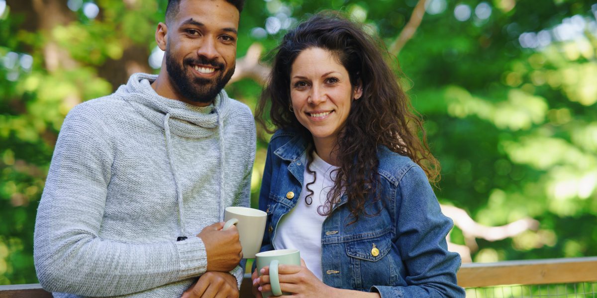 A happy couple resting and looking at camera outdoors in a tree house, weekend away and digital detox concept.