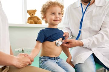 Portrait of adorable little boy visiting doctor, looking brave and smiling, holding mothers hand while pediatrician listening to heartbeat with stethoscope