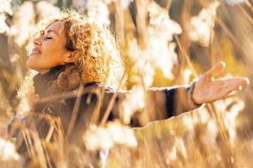 One happy woman outstretching arms and enjoying nature smiling in golden field with sunset sunlight. People and outdoor leisure activity. Happiness and wellbeing lifestyle lady. Freedom. Overjoy life