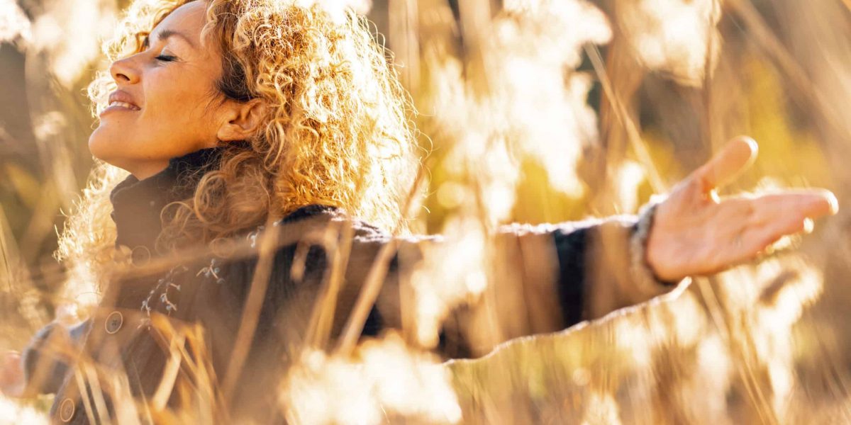 One happy woman outstretching arms and enjoying nature smiling in golden field with sunset sunlight. People and outdoor leisure activity. Happiness and wellbeing lifestyle lady. Freedom. Overjoy life