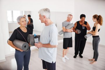 Senior couple with exercise mats talking to each other after yoga class with other people in the background