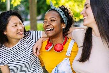 Three united multi-ethnic female friends having fun laughing together outdoor. Young adult group of millennial women laughing while enjoying day off