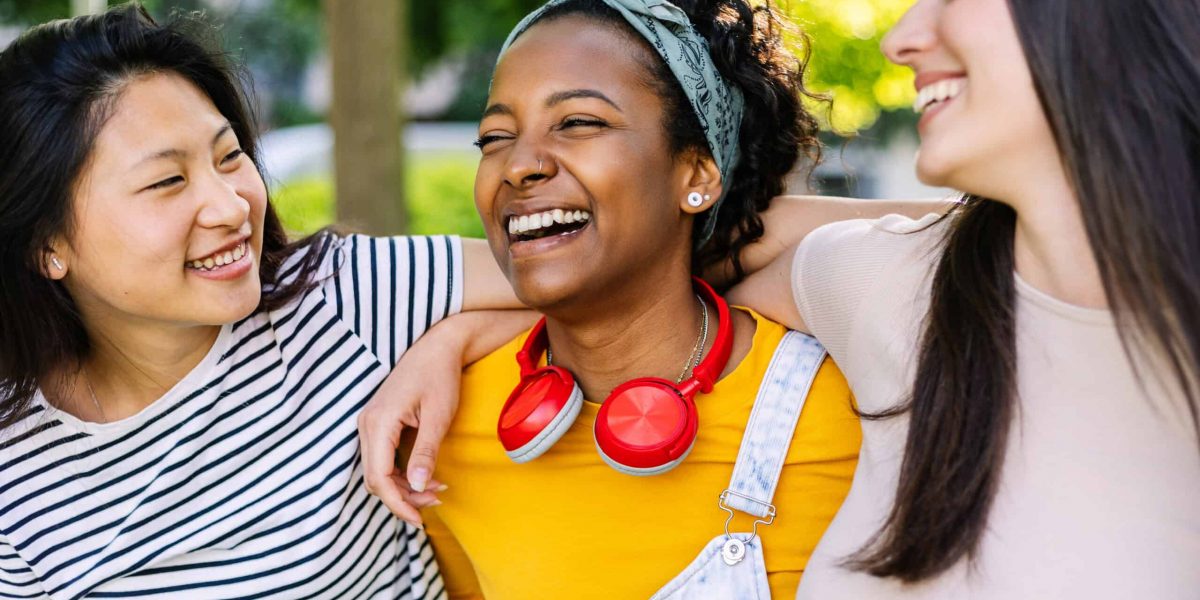 Three united multi-ethnic female friends having fun laughing together outdoor. Young adult group of millennial women laughing while enjoying day off