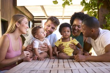 Two Families With Young Children At Table Outdoors At Home
