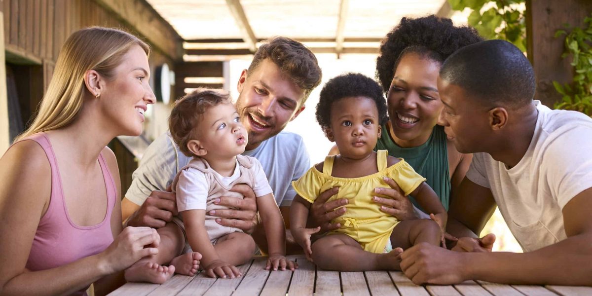 Two Families With Young Children At Table Outdoors At Home